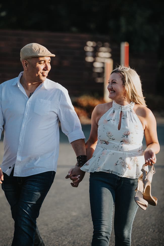 The couple walking and smiling at each other, holding hands and shoes, in a relaxed setting.