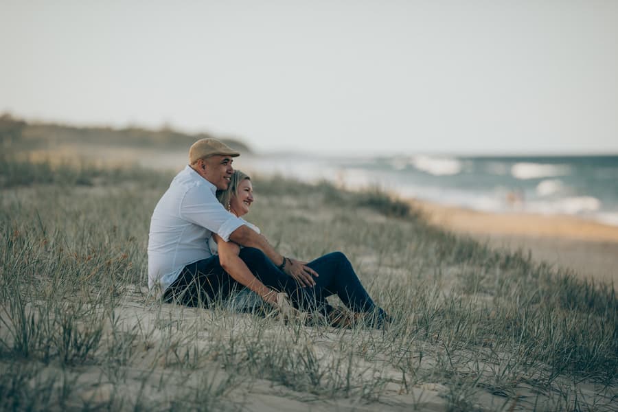The couple sitting on the beach at Novotel Twin Waters, embracing and looking towards the ocean.