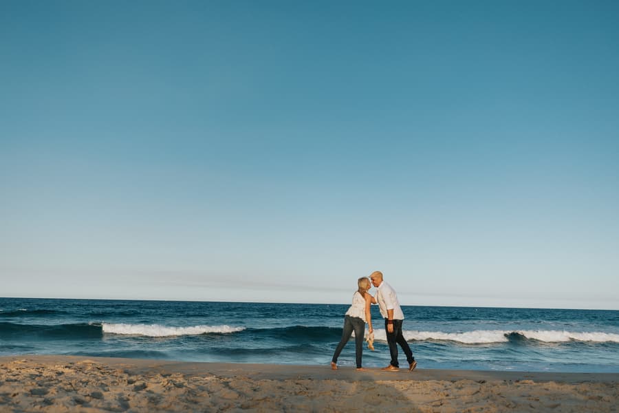 The couple standing on the beach, leaning in for a kiss, under a vast blue sky.