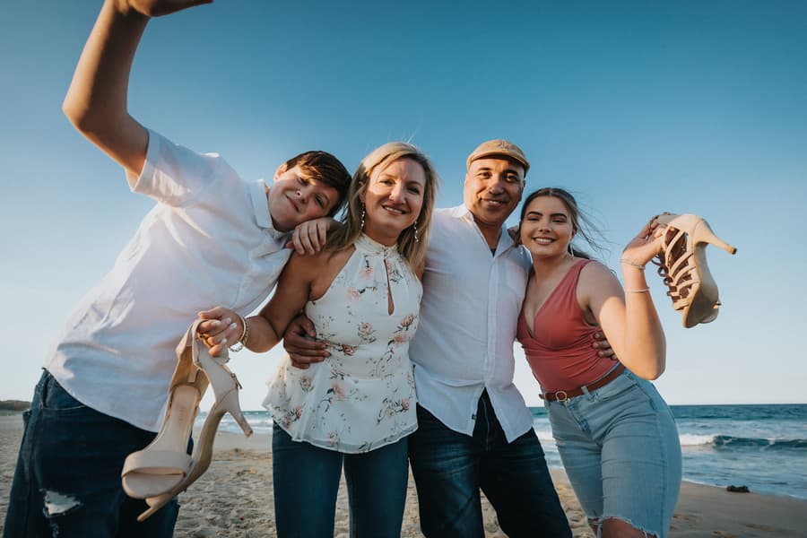 The couple with two others, all smiling and holding shoes, enjoying a moment on the beach.