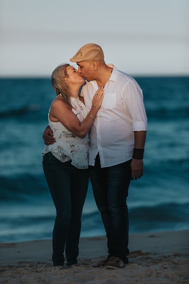 The couple sharing a kiss on the beach with the ocean in the background at Novotel Twin Waters.