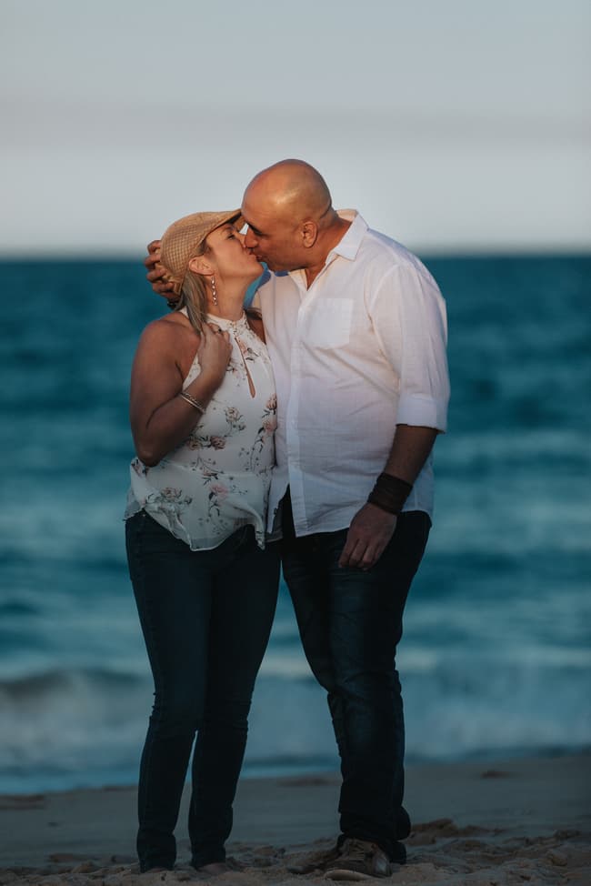 The couple kissing on the beach, with the man wearing a hat, at Novotel Twin Waters.