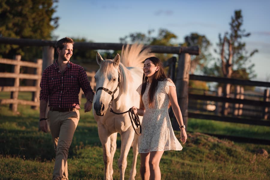 The couple walking a white horse on a grassy field, both smiling in the afternoon light.
