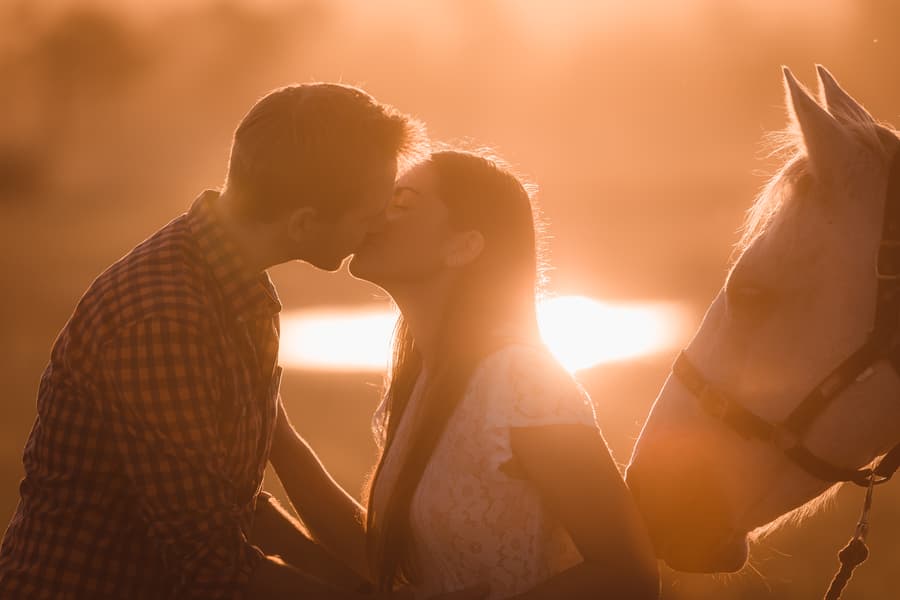 The couple kissing with a horse beside them, bathed in the warm light of sunset.