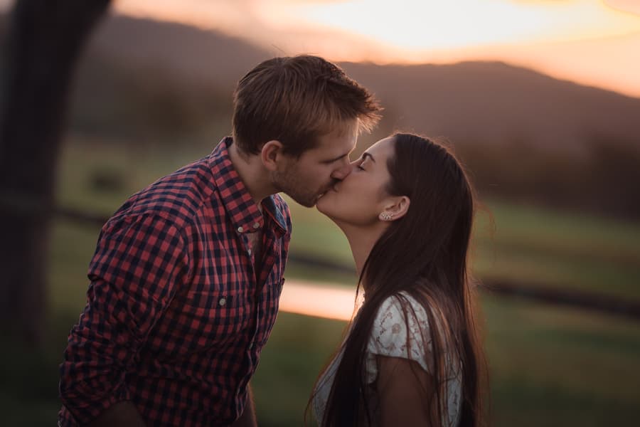 The couple kissing with a scenic sunset and hills in the background.