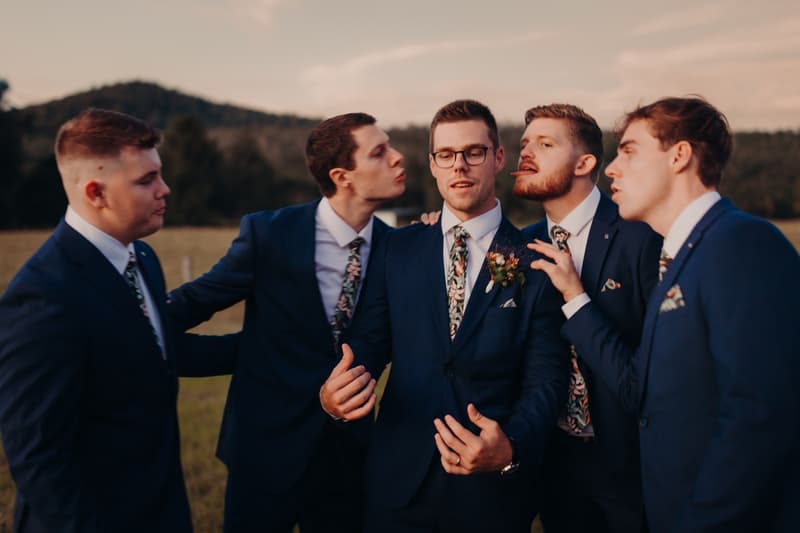 Connor, the groom, stands with four groomsmen outdoors at Yabbaloumba Retreat, all wearing matching navy suits and floral ties.
