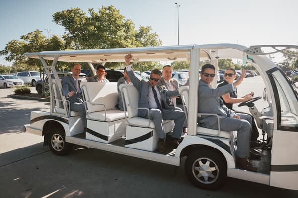 Groom Dane and groomsmen dressed in suits ride in a white open-sided shuttle vehicle. Shortest day wedding timeline by She Said Yes.