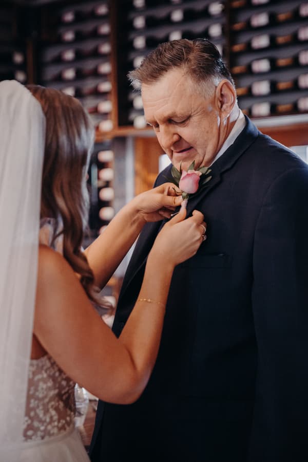 The bride Chelsea pins a pink rose boutonniere onto an older man, likely her father, at Preston Peak Winery Functions Centre.