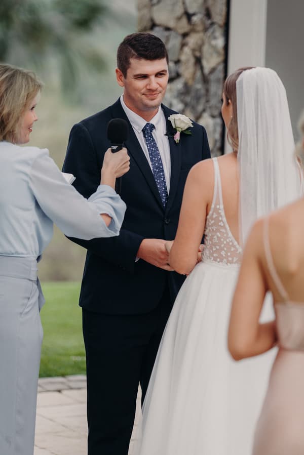 Brent and Chelsea hold hands during their wedding ceremony at Preston Peak Winery Functions Centre, with the officiant holding a microphone.