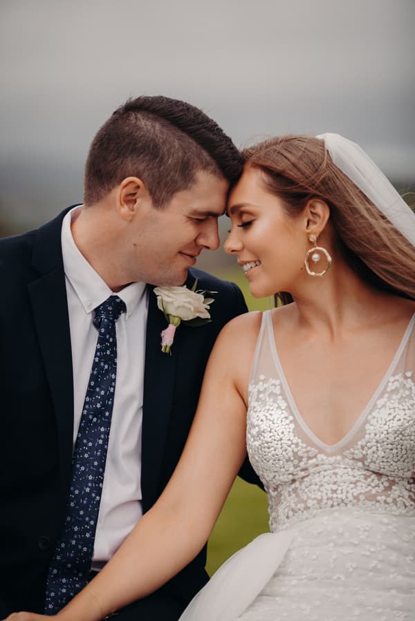 Bride Chelsea and groom Brent touch foreheads in a close-up portrait at Preston Peak Winery Functions Centre, with Chelsea wearing a white wedding dress and veil and Brent in a dark suit with a floral tie and white boutonniere.