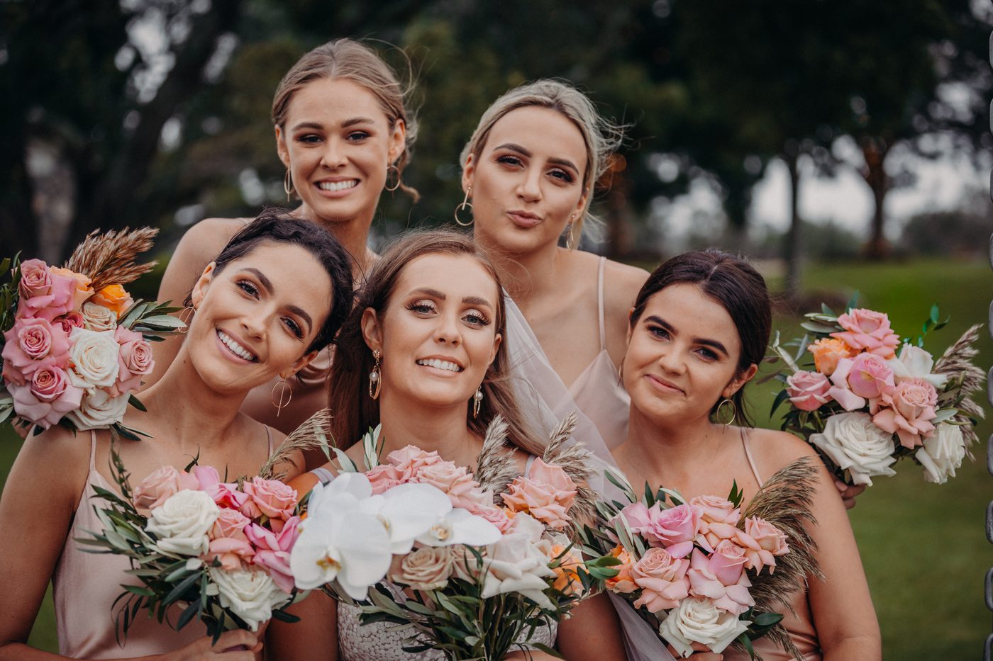 Five bridesmaids pose together outdoors, each holding bouquets of pink, white, and peach flowers with greenery. Elopement photography Brisbane by She Said Yes.