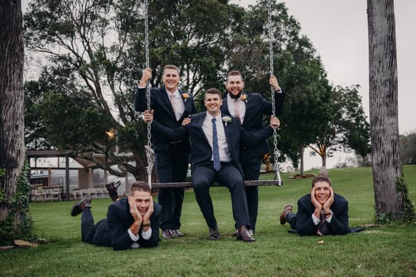 Brent sits on a swing held by two men in suits while two other men lie on the grass in front of them at Preston Peak Winery Functions Centre.