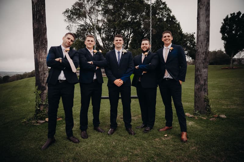 Brent and four groomsmen stand on grass between two wooden posts with a swing at Preston Peak Winery Functions Centre.