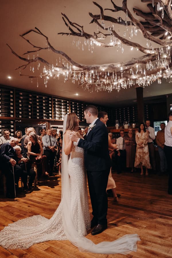 Bride Chelsea and groom Brent share their first dance at Preston Peak Winery Functions Centre with guests watching in the background under a decorative chandelier.