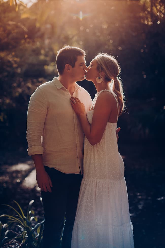 The couple kisses softly in the Brisbane Botanic Gardens, bathed in warm, golden sunlight.