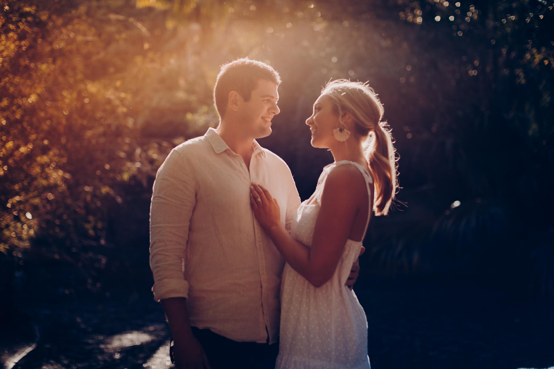 The couple gazes at each other lovingly, standing in the Brisbane Botanic Gardens with sunlight illuminating their faces.