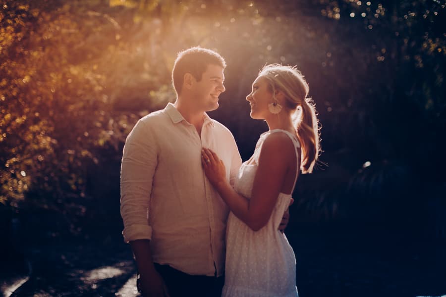 The couple gazes at each other lovingly, standing in the Brisbane Botanic Gardens with sunlight illuminating their faces.