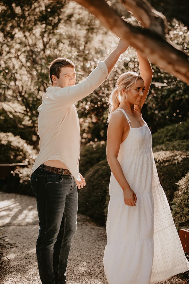 The couple stands close together, with one partner twirling the other under a tree in the Brisbane Botanic Gardens.