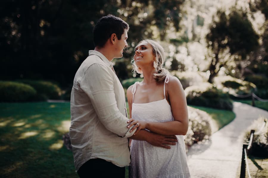 The couple stands close, gazing at each other lovingly in the Brisbane Botanic Gardens, with a winding path behind them.