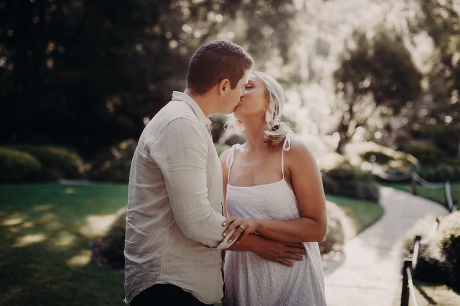The couple shares a kiss in a sunlit garden, surrounded by lush greenery at Brisbane Botanic Gardens.