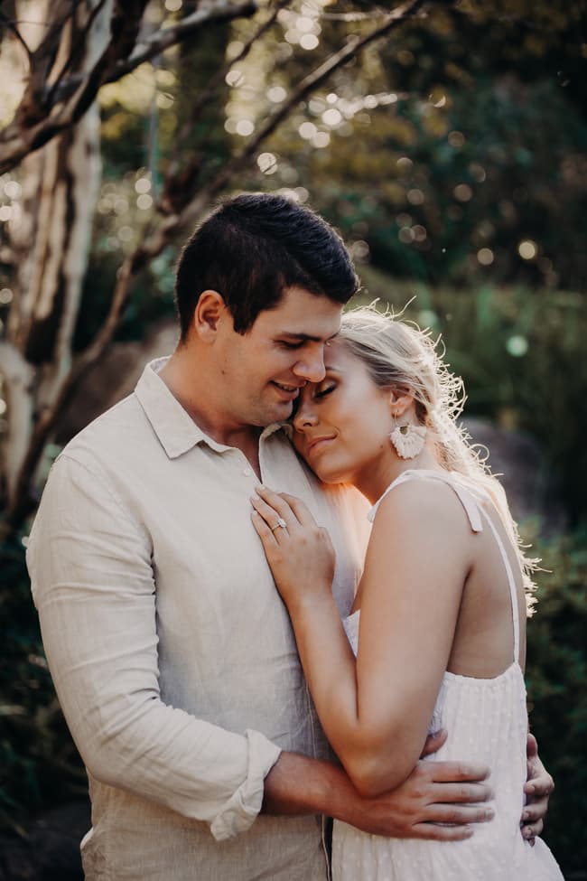 The couple shares an intimate moment, with one resting their head on the other's shoulder in the garden.