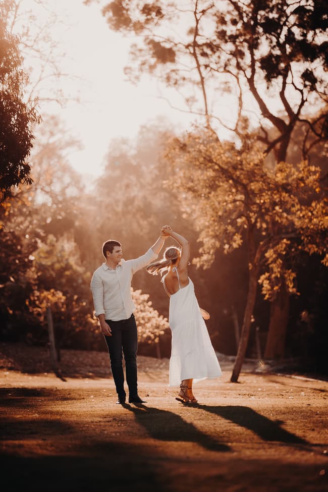 The couple dances on a grassy area, twirling under the warm afternoon sun.
