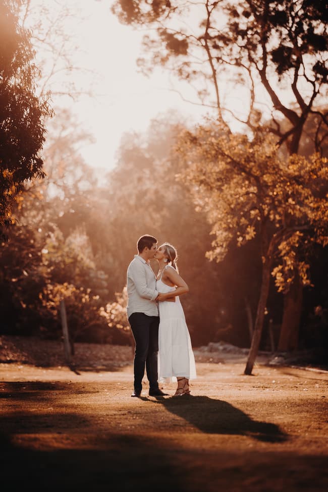 The couple shares a gentle kiss, standing close together in a sunlit garden.