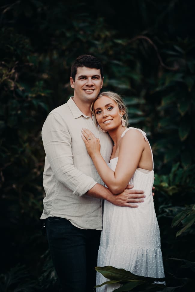 The couple stands closely together, smiling softly, surrounded by lush greenery at Brisbane Botanic Gardens.