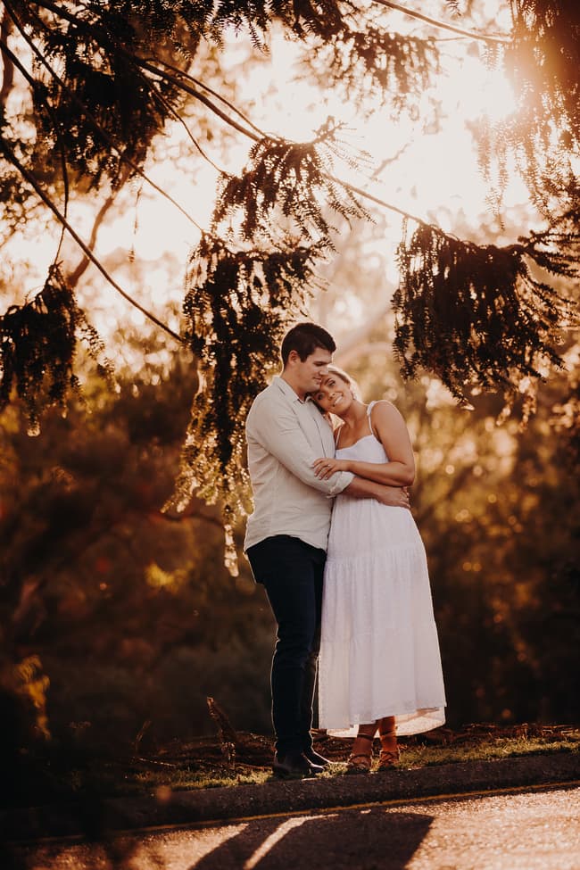 The couple stands close, bathed in warm sunlight filtering through trees at Brisbane Botanic Gardens.