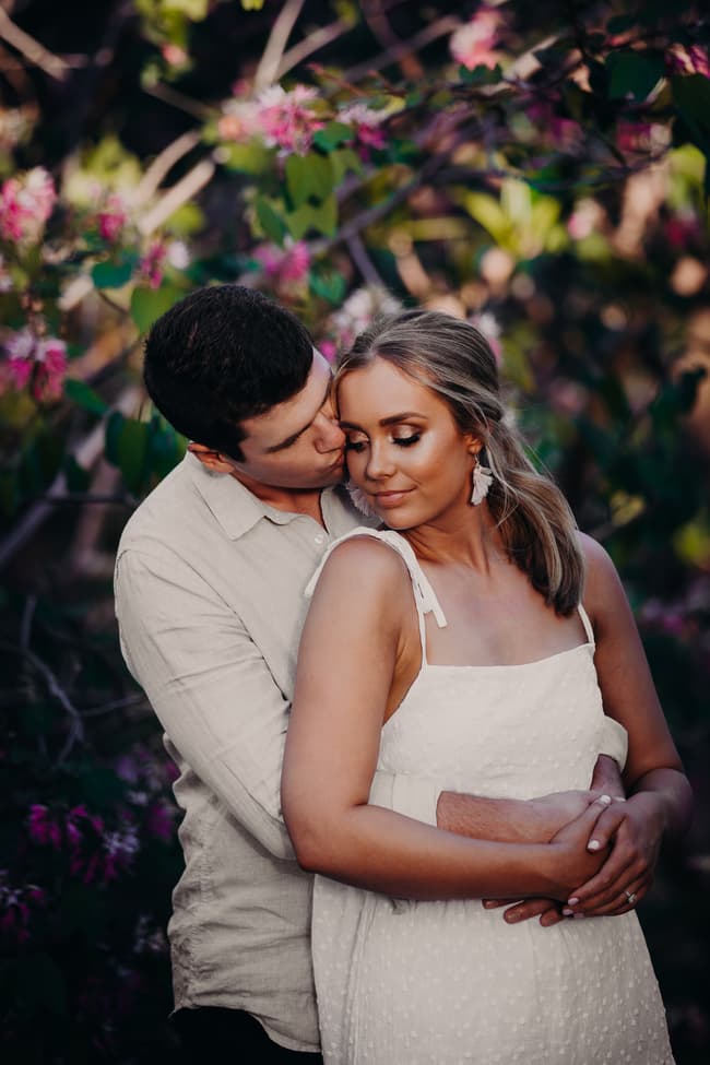 The couple shares an intimate moment, with one leaning in for a gentle kiss on the other's cheek.