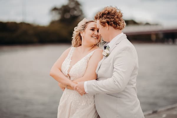 The bride Chloe and groom Brodie embrace and smile at each other near the water.