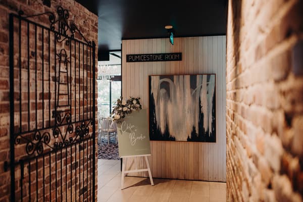 Entrance to the Pumicestone Room at Sandstone Point Hotel with a wedding welcome sign for Chloe and Brodie displayed on an easel decorated with flowers.