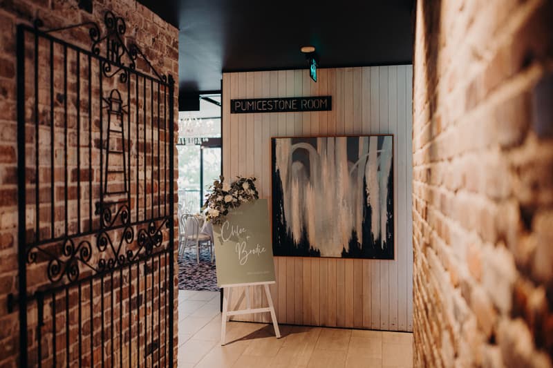 Entrance to the Pumicestone Room at Sandstone Point Hotel with a wedding welcome sign for Chloe and Brodie displayed on an easel decorated with flowers.