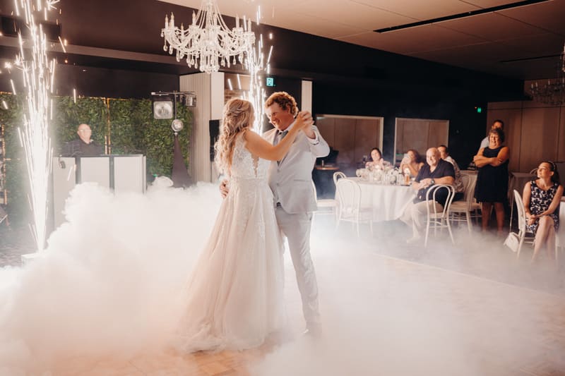 The bride Chloe and groom Brodie share their first dance surrounded by low fog and sparklers, with seated and standing guests watching in the background. Cinematic videography wedding by She Said Yes.