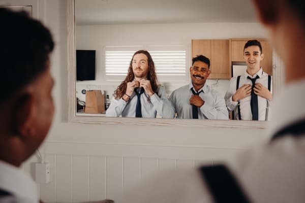 Three groomsmen adjust their ties while looking into a mirror in a room at Sandstone Point Hotel.
