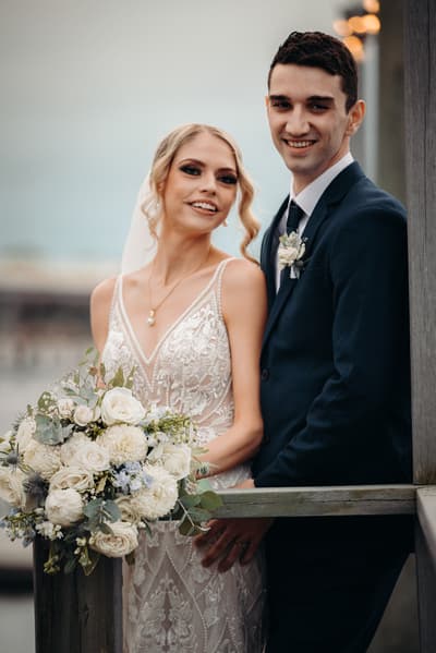 Courtney the bride and Cameron the groom pose together holding a bouquet of white flowers. Australian wedding photographer by She Said Yes.