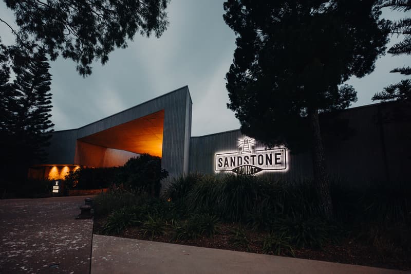 Exterior view of Sandstone Point Hotel entrance at dusk with illuminated signage and surrounding trees and plants.