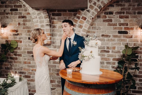 Courtney, the bride, feeds a piece of wedding cake to Cameron, the groom, at the reception stage in Sandstone Point Hotel — Cellar.