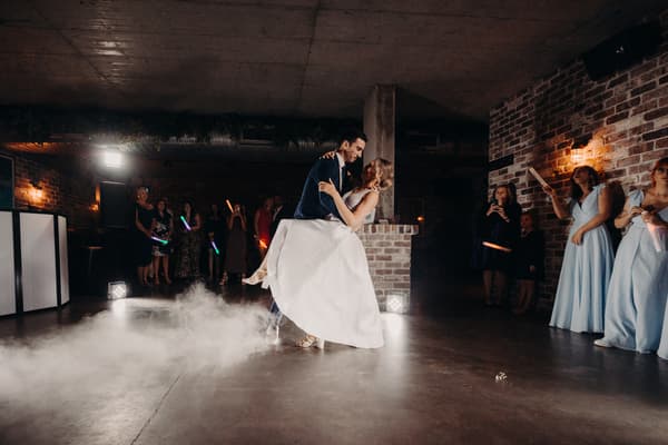 Courtney and Cameron share a dance on the reception stage at Sandstone Point Hotel — Cellar, surrounded by guests and bridesmaids holding glow sticks.