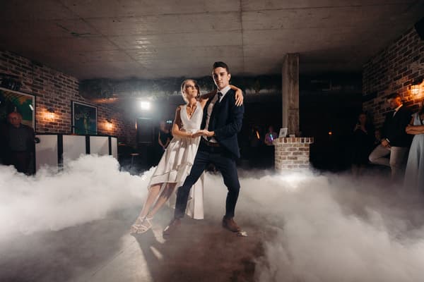 Courtney the bride and Cameron the groom dance on the reception stage at Sandstone Point Hotel — Cellar with low fog surrounding them and guests watching in the background.