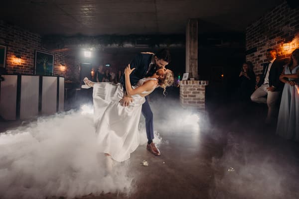 Courtney and Cameron share a kiss on the dance floor during their first dance at the Sandstone Point Hotel — Cellar, surrounded by guests and low-lying fog effects.