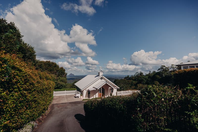 Exterior view of Tiffany's Maleny Chapel surrounded by greenery under a blue sky with clouds.