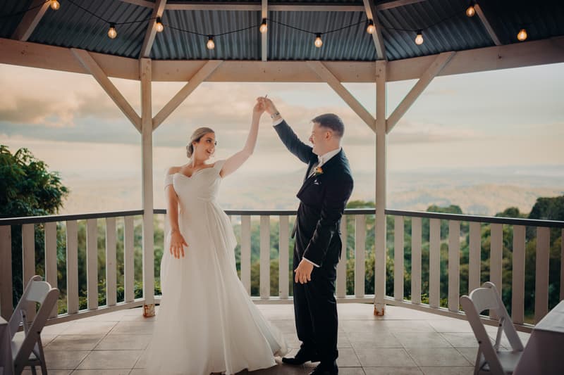 Courtney the bride and Liam the groom dance together under a gazebo at Tiffany's Maleny with a scenic view of trees and hills in the background.