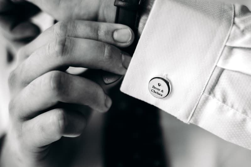 Close-up of the groom's hands adjusting a cufflink engraved with 'Brent & Chelsea' on a white dress shirt at Preston Peak Winery Functions Centre.