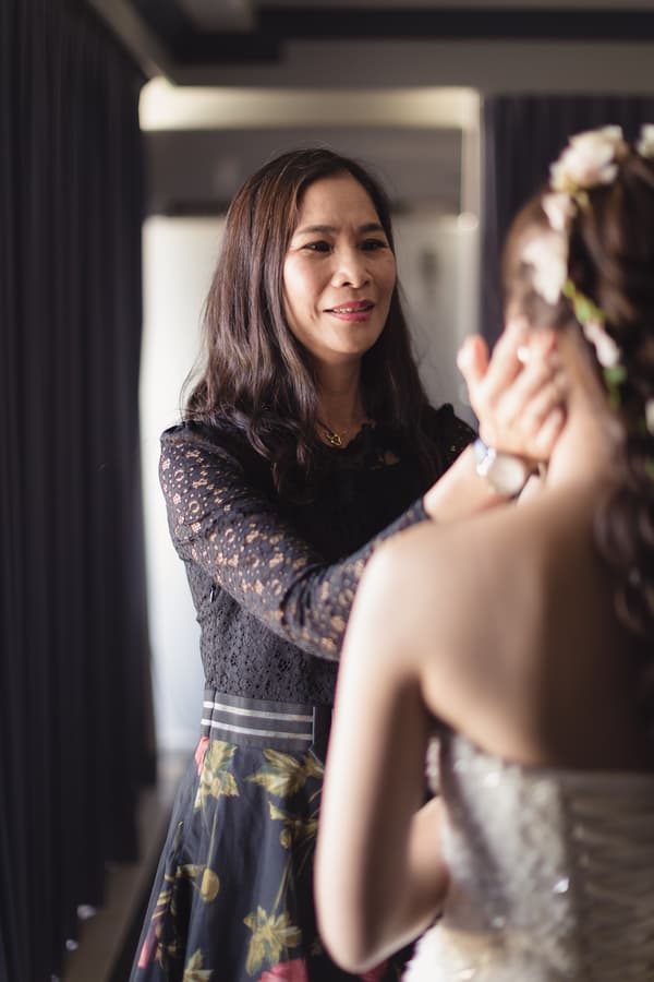 The bride's mother gently touches the bride's face indoors during bridal preparation.