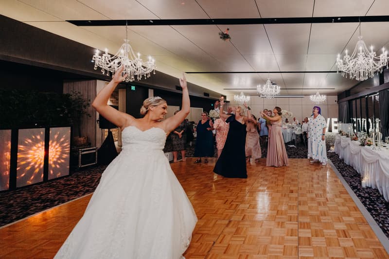 The bride throws her bouquet to a group of female guests at the reception in the Pumicestone Room at Sandstone Point Hotel.