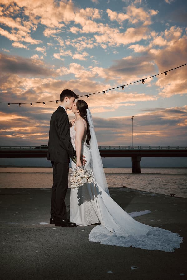 Terion and Tyler share a kiss during a styled portrait session at Sandstone Point Hotelallo at sunset, with string lights overhead and a bridge in the background.