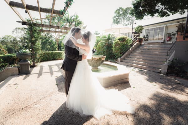 Pasha and Maryam embrace under a pergola near a fountain at Hillstone St Lucia — The Quartyard during a styled portrait session.