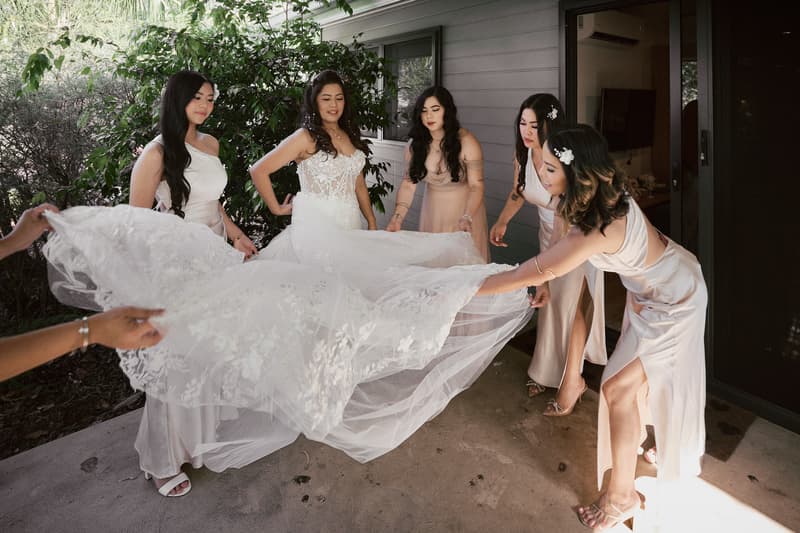 The bride Jheng stands outside a building at Sandstone Point Hotel while bridesmaids adjust the train of her wedding dress.
