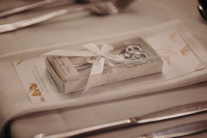 A wedding favor box tied with a white ribbon is placed on a folded napkin atop a table setting at Sandstone Point Hotel — Pumicestone Room.